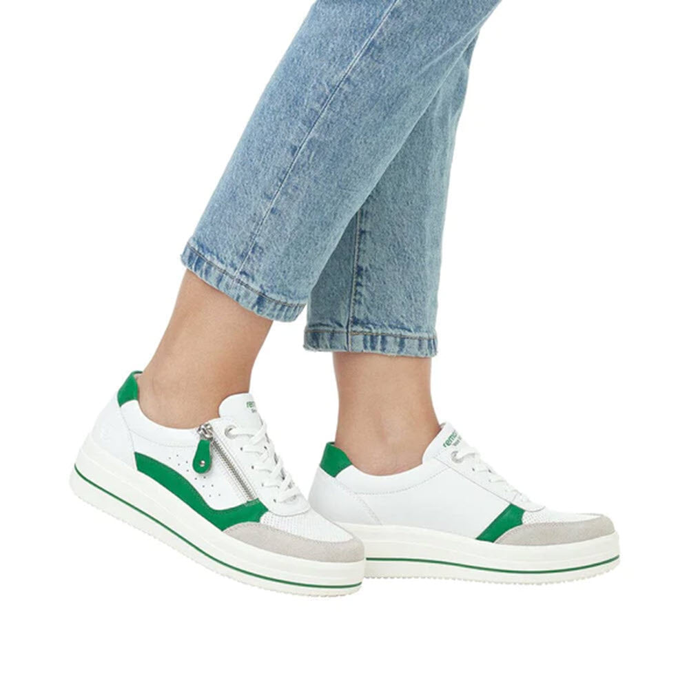 A person wearing light blue jeans and white sneakers with green accents, Remonte REMONTE EURO COURT SNEAKER GRASS GREEN - WOMENS, built for intensive wear.