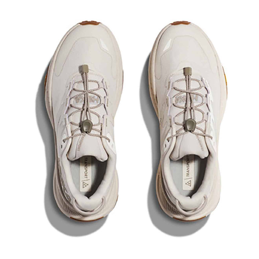 A pair of Hoka TRANSPORT EGGNOG/EGGNOG athletic sneakers with beige accents and Vibram® EcoStep Natural outsole, viewed from above, isolated on a white background.