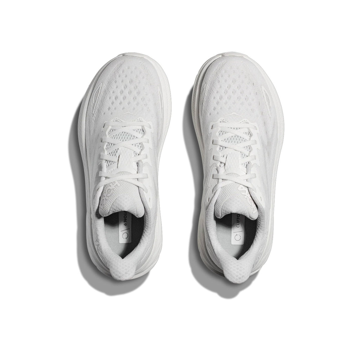A pair of white Hoka Clifton 9 running shoes seen from above, featuring an improved outsole design.