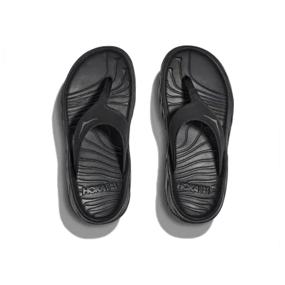 A pair of black HOKA ORA Recovery Flip flops by Hoka with contoured footbeds and oversized midsole, displayed on a white background.