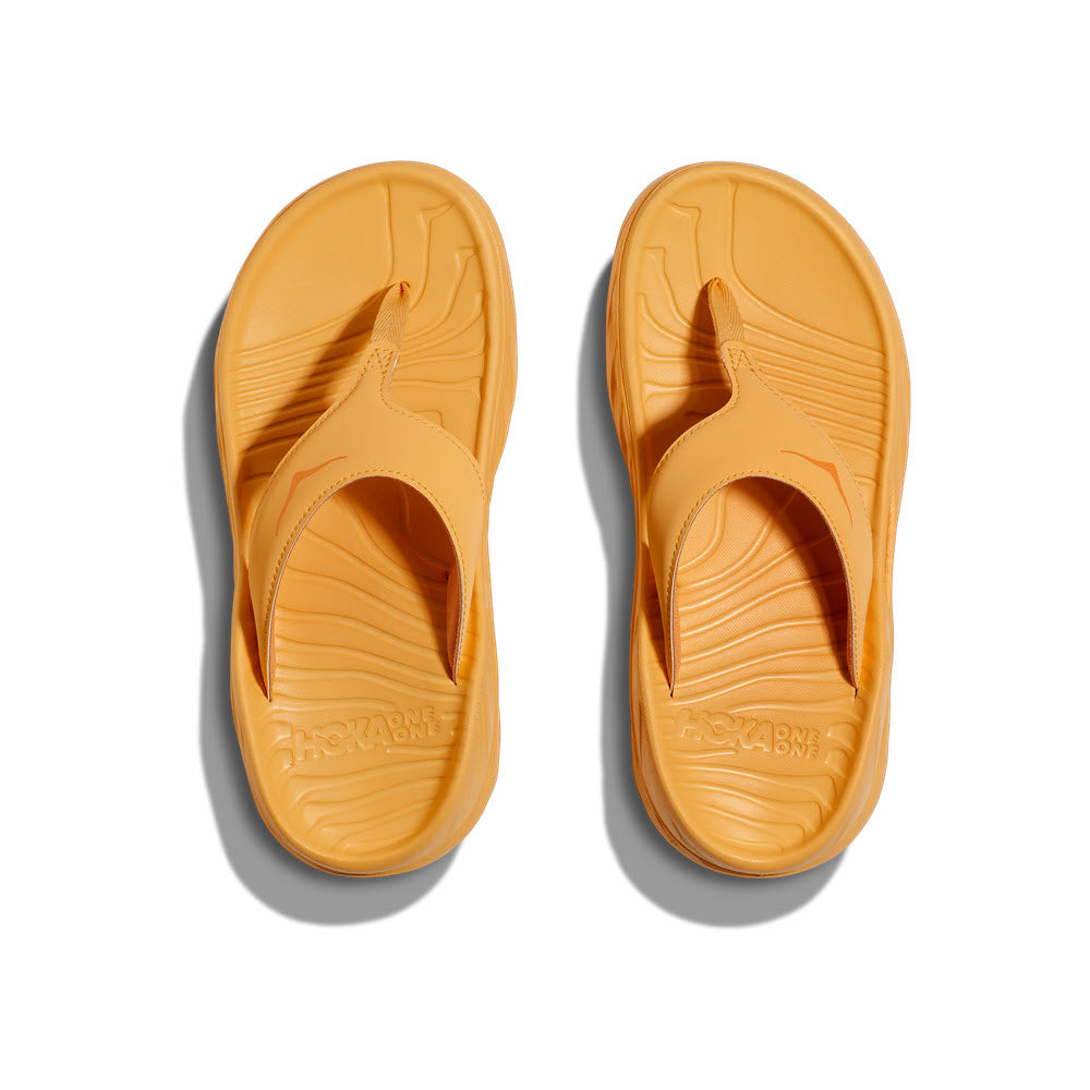 A pair of yellow HOKA ORA RECOVERY FLIP flip-flops on a white background, viewed from above.