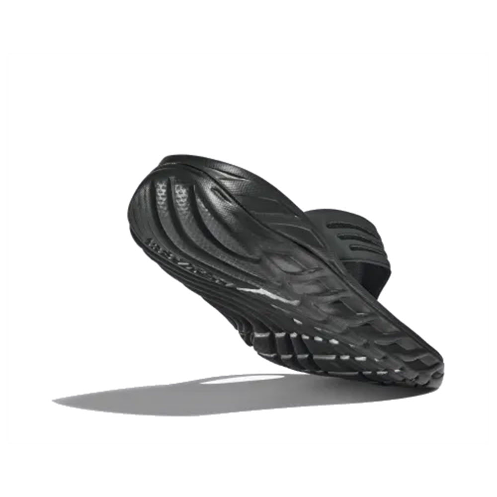A pair of Hoka Ora Recovery Flip Black/Dark Gull Gray men&#39;s athletic shoes featuring soft cushioning, floating in mid-air against a plain white background.