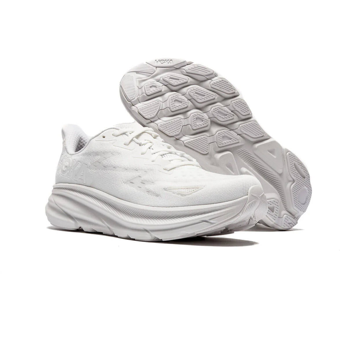 A pair of white Hoka CLIFTON 9 running shoes displayed with one shoe flipped to show the improved outsole design.
