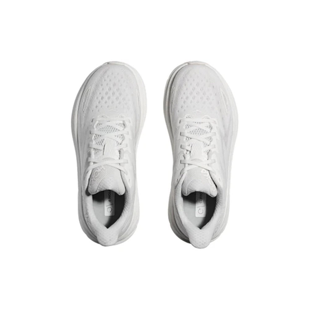 A pair of white Hoka Clifton 9 running shoes viewed from above, displaying laces and breathable mesh fabric on a white background with improved outsole design.
