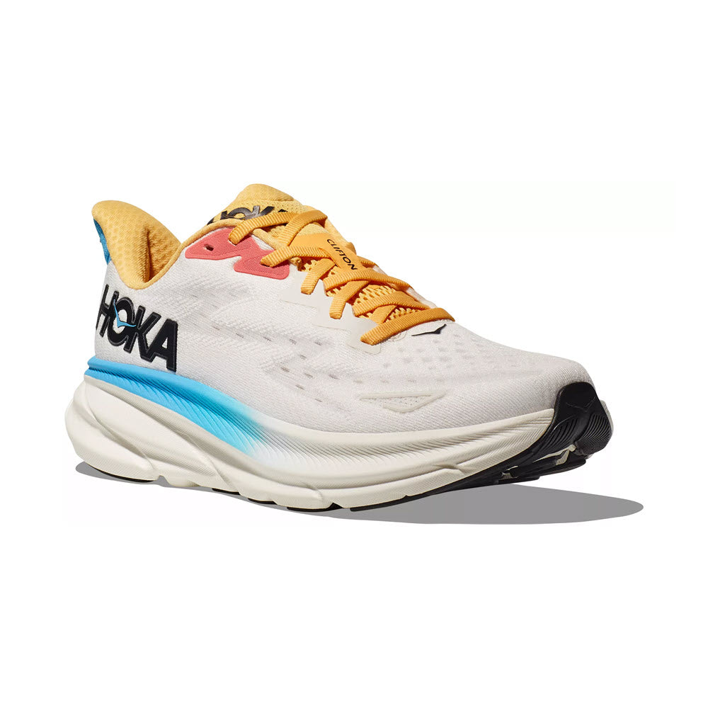 Side view of a white Hoka Clifton 9 Blanc de Blanc/Swim Day running shoe with yellow laces, blue and black accents, and the Hoka brand name visible on the side.