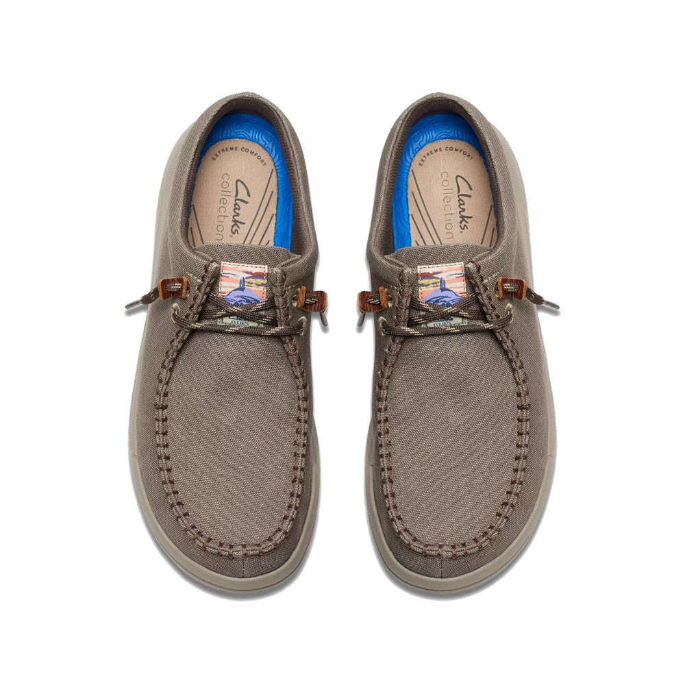 Top view of a pair of Clarks Driftlite Surf Slip On Moc Toe Taupe Interest boat shoes with brown leather laces and blue insoles, featuring an Extreme Comfort foam footbed, isolated on white background.