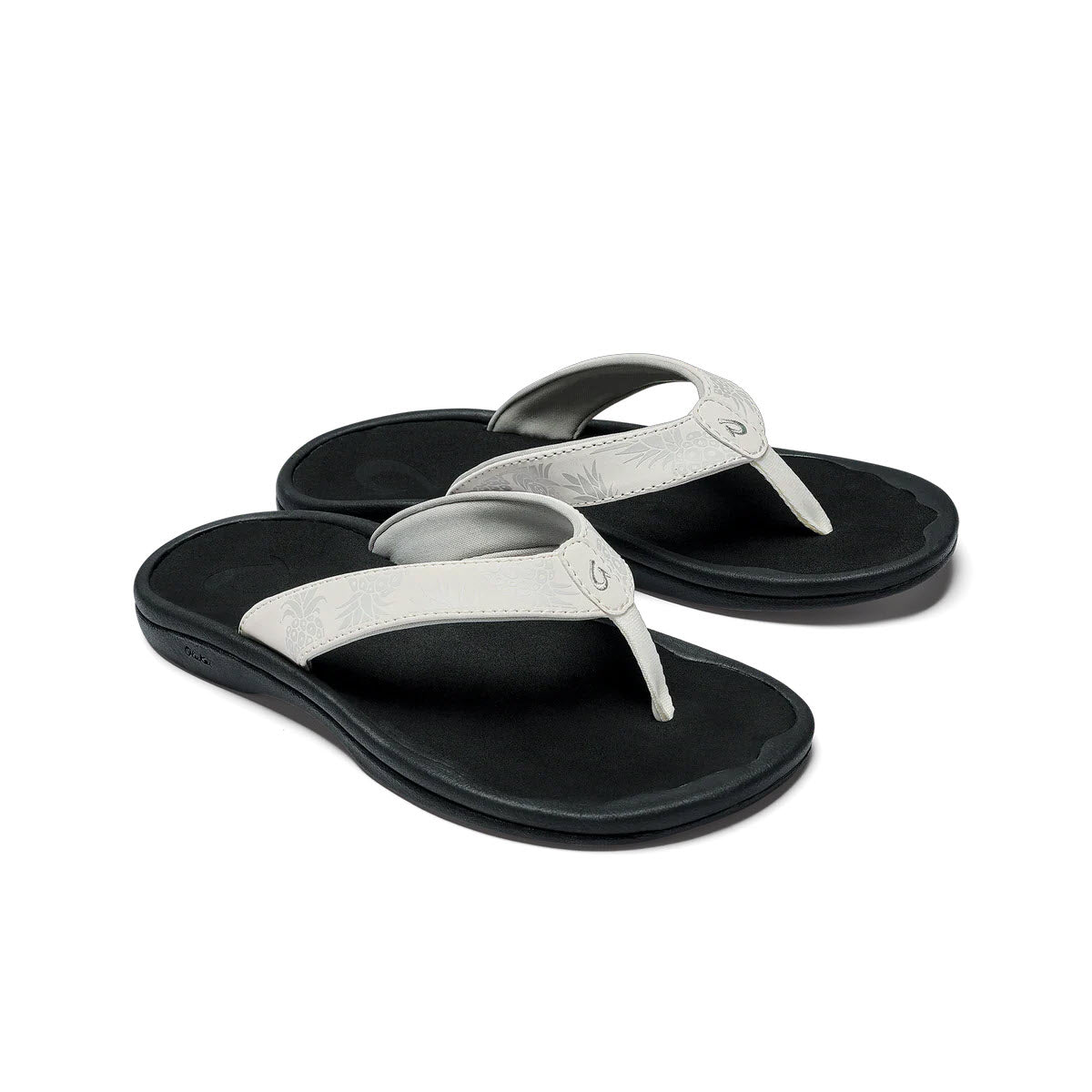 A pair of black, water-resistant flip-flops with silver embellishments on the straps, isolated on a white background. Made by Olukai Ohana Bright White - Womens.