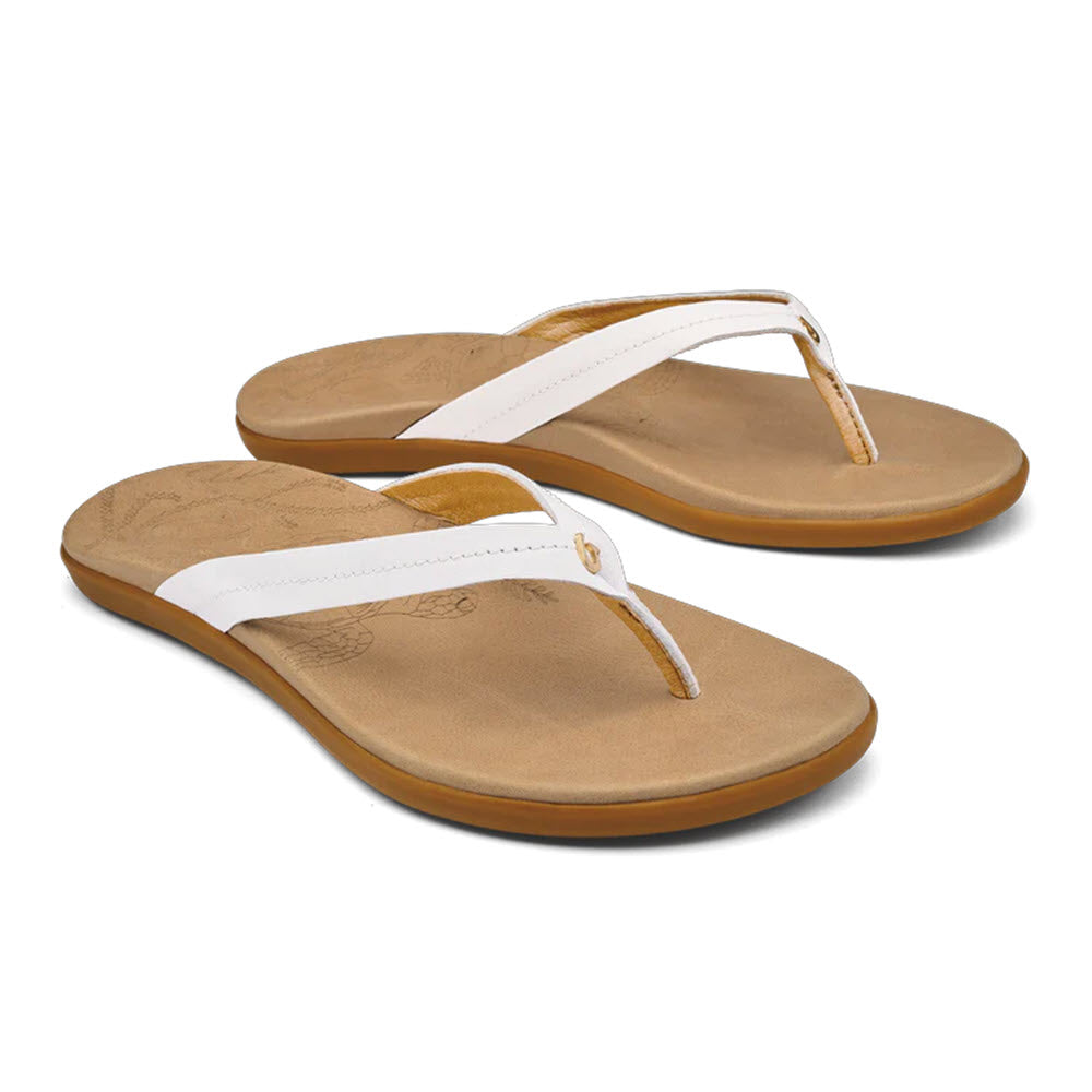 A pair of white Olukai Honu Bright White flip-flops with leather footbeds and tan soles isolated on a white background.