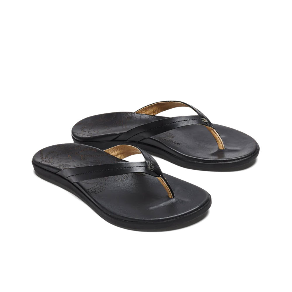 A pair of Olukai Honu Black women&#39;s flip-flops with gold accents and a laser-etched Hawaiian Green Sea Turtle design on a white background.