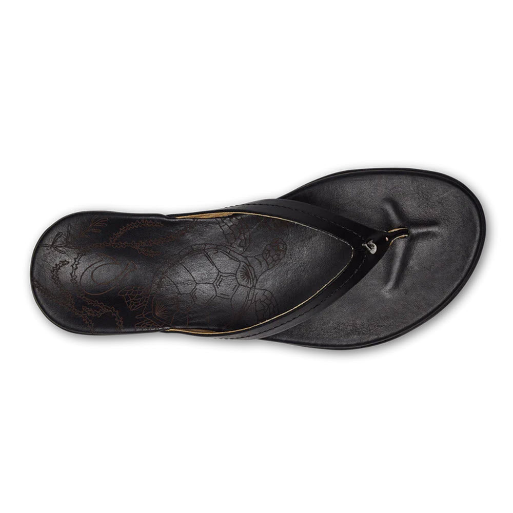 A pair of OLUKAI HONU BLACK flip-flops with a laser-etched, patterned insole on a white background.