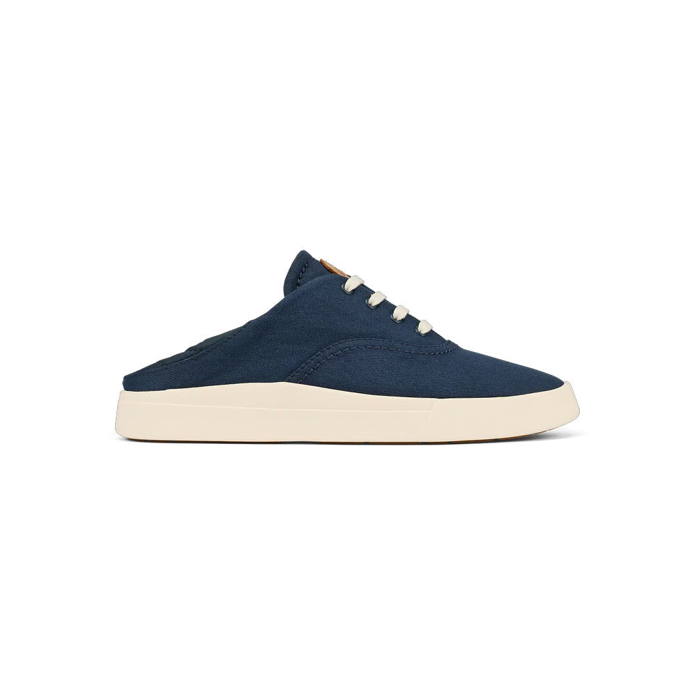 Side view of a Olukai navy blue minimalist sneaker with white laces and a cream-colored sole, isolated on a white background.