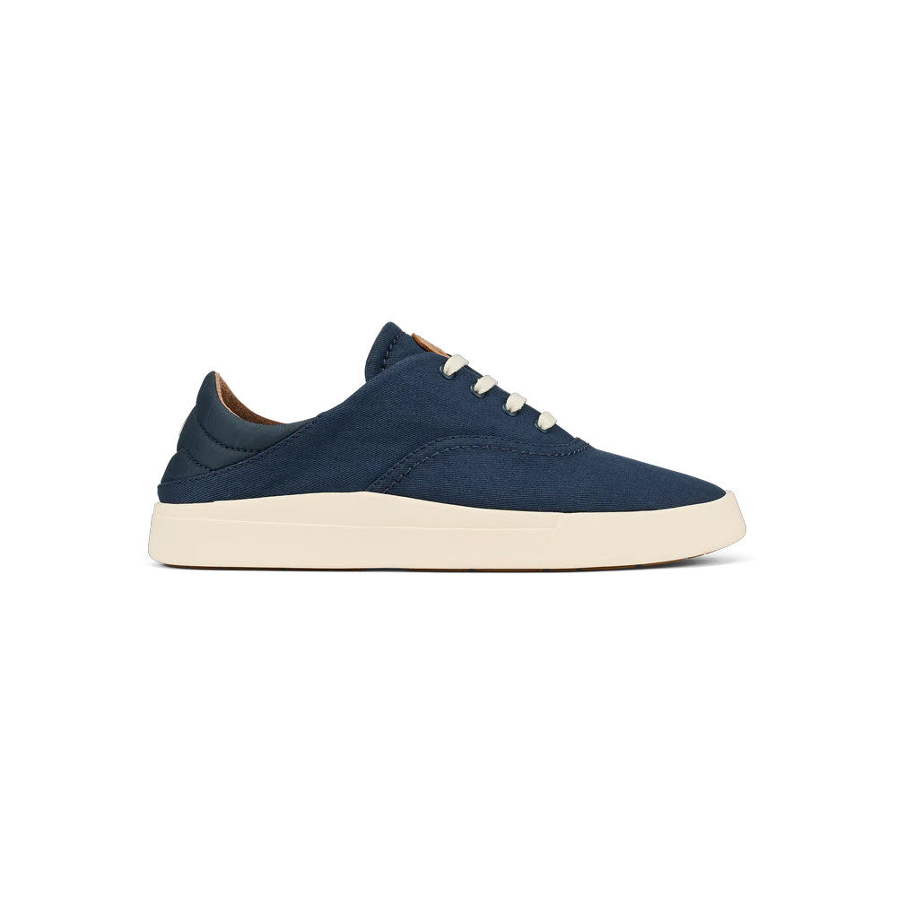A Olukai navy blue minimalist sneaker with white laces and a beige sole, displayed against a white background.