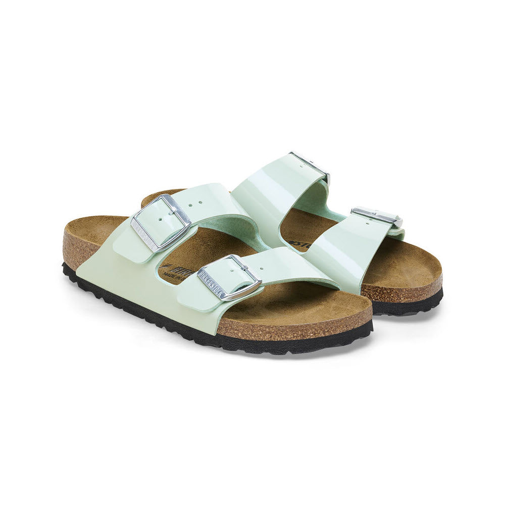 A pair of Birkenstock Arizona Patent Surf Green sandals with buckle closures and a cork footbed, isolated on a white background.