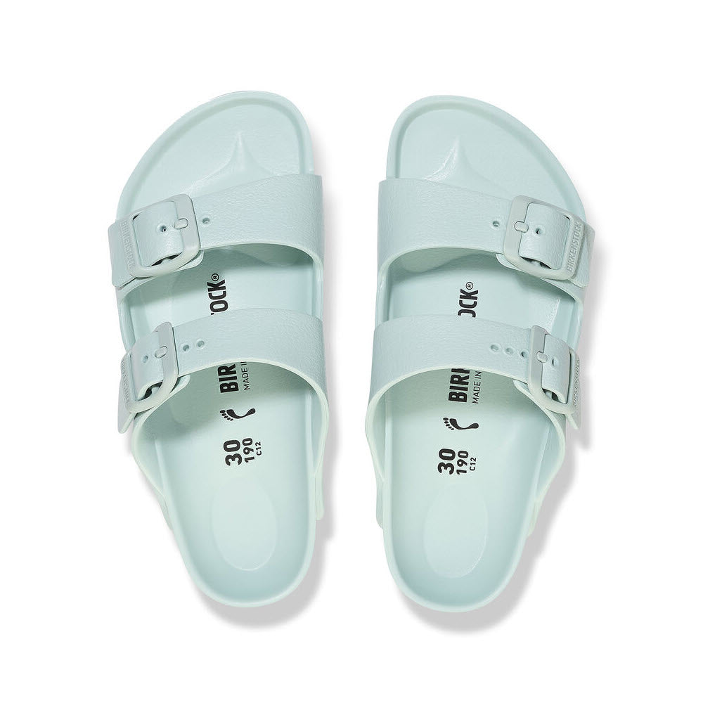 A pair of pale green Birkenstock Arizona EVA Surf Green - Kids sandals with two buckles on each, viewed from above on a white background.