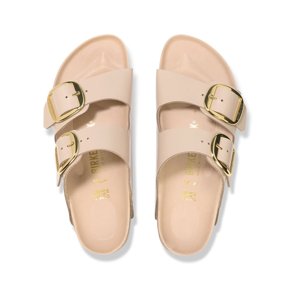A pair of beige Birkenstock Arizona Big Buckle High Shine New Beige sandals with golden buckles, viewed from above, isolated on a white background.