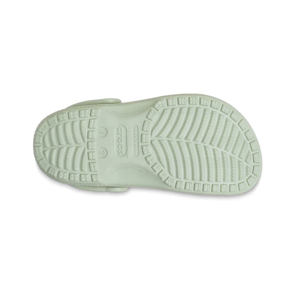 Bottom view of a light green Crocs Classic Clog Plaster for kids shoe showing the tread pattern and brand imprint.