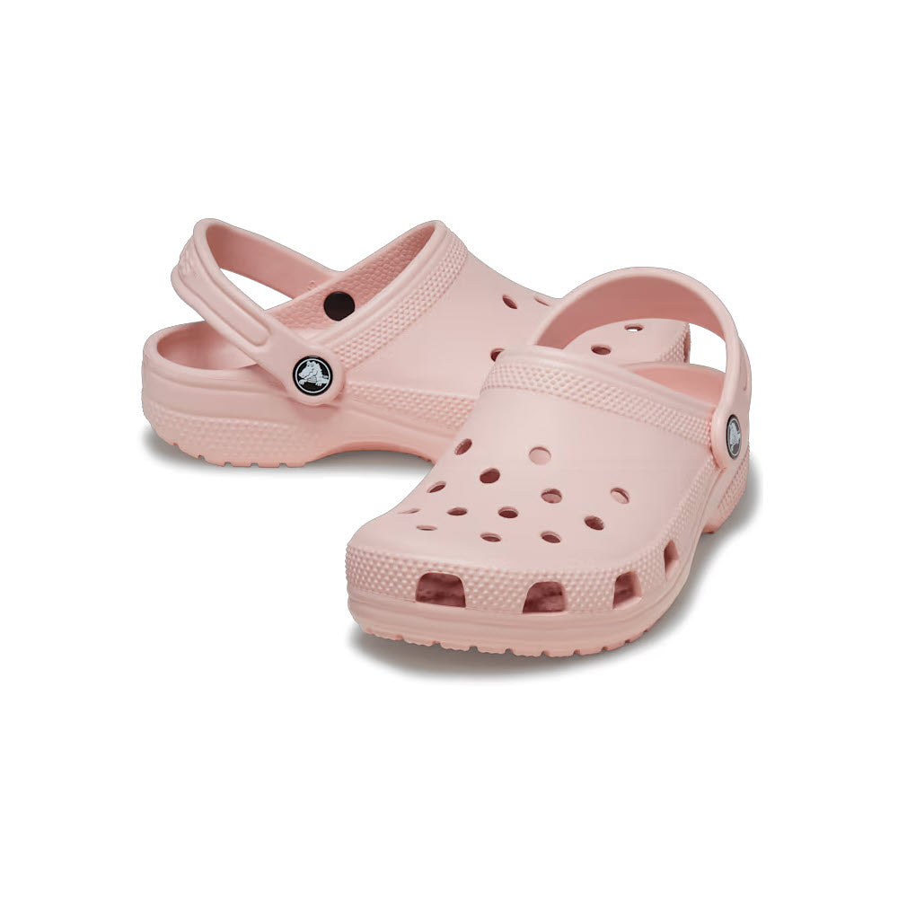 A pair of pink kids Crocs Classic Clog Quartz, adorned with Jibbitz charms, on a white background.