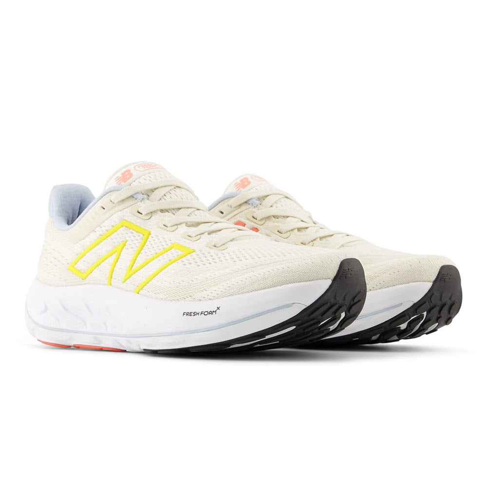 A pair of NEW BALANCE VONGO V6 SEA SALT/LEMON ZEST/LIGHT CHROME - WOMENS running shoes in white with a prominent yellow &quot;n&quot; logo on the side, designed for a cushioned ride.
