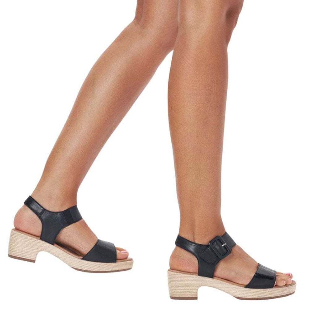 A close-up of a person wearing Remonte block heel sandal black - womens by Remonte, showcasing only their lower legs and feet.