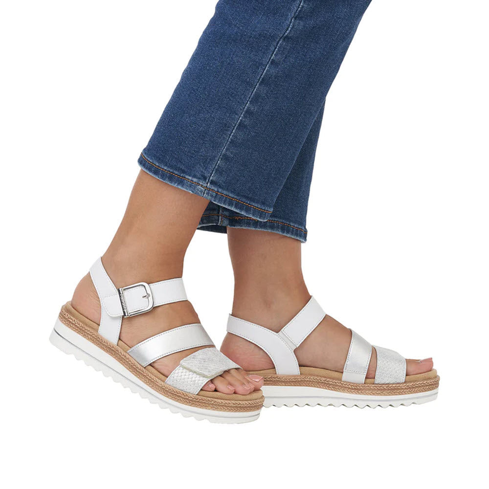 A person wearing Remonte City Walker Gladiator Sandals in white with Velcro closure and blue cropped jeans, standing against a white background.