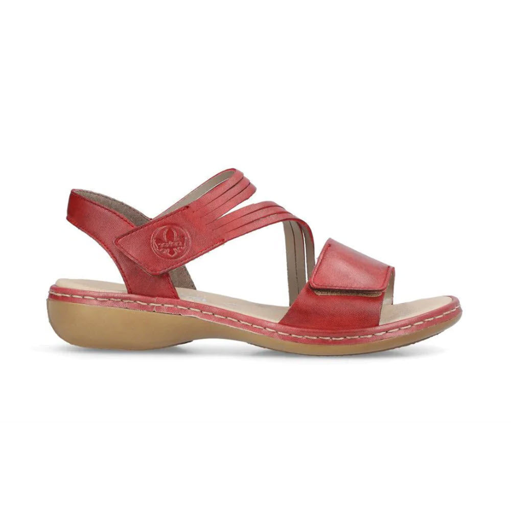 A red smooth leather sandal with a low wedge heel, featuring an adjustable hook and loop fastener and a round emblem on the side, displayed against a white background. - RIEKER COMFORT BOTTOM ASYMMETRICAL SANDAL RED by Rieker