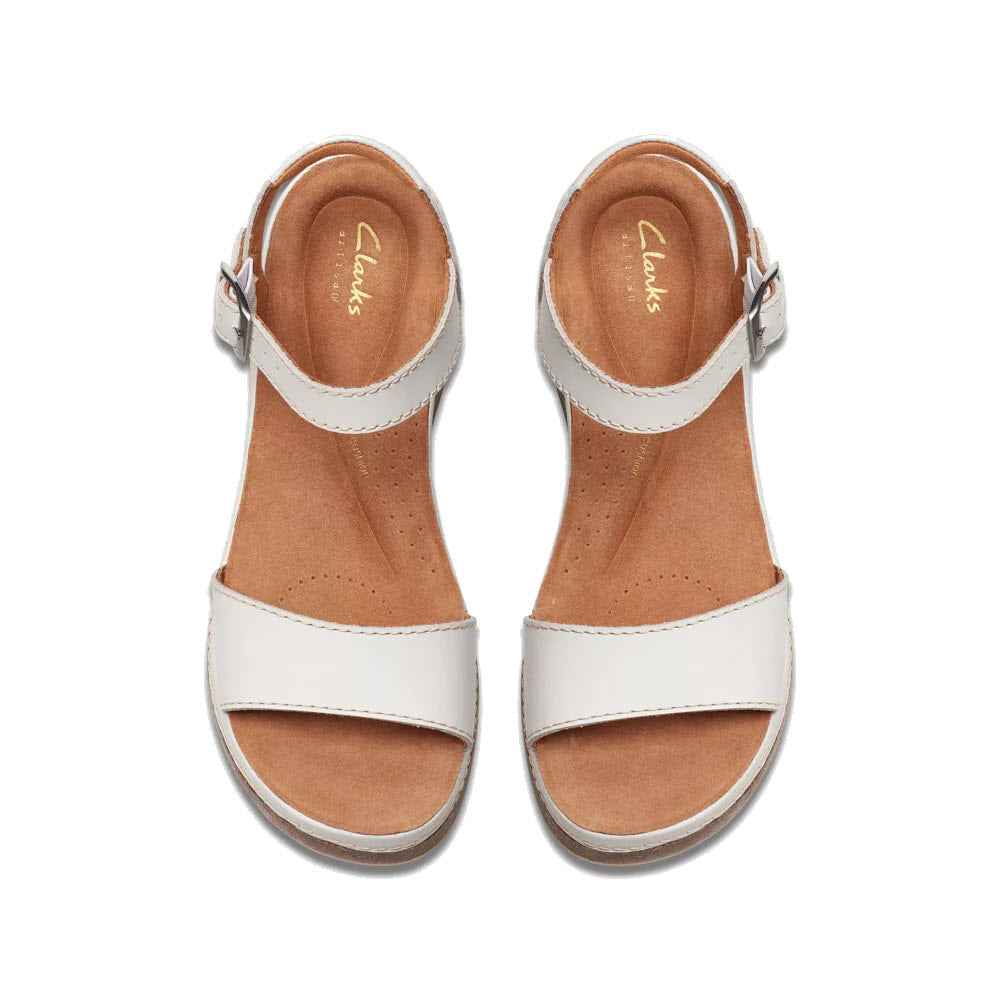 A pair of white Clarks Kassanda Lily OFF WHITE - WOMENS sandals with ankle straps and brown insoles, viewed from above on a white background.