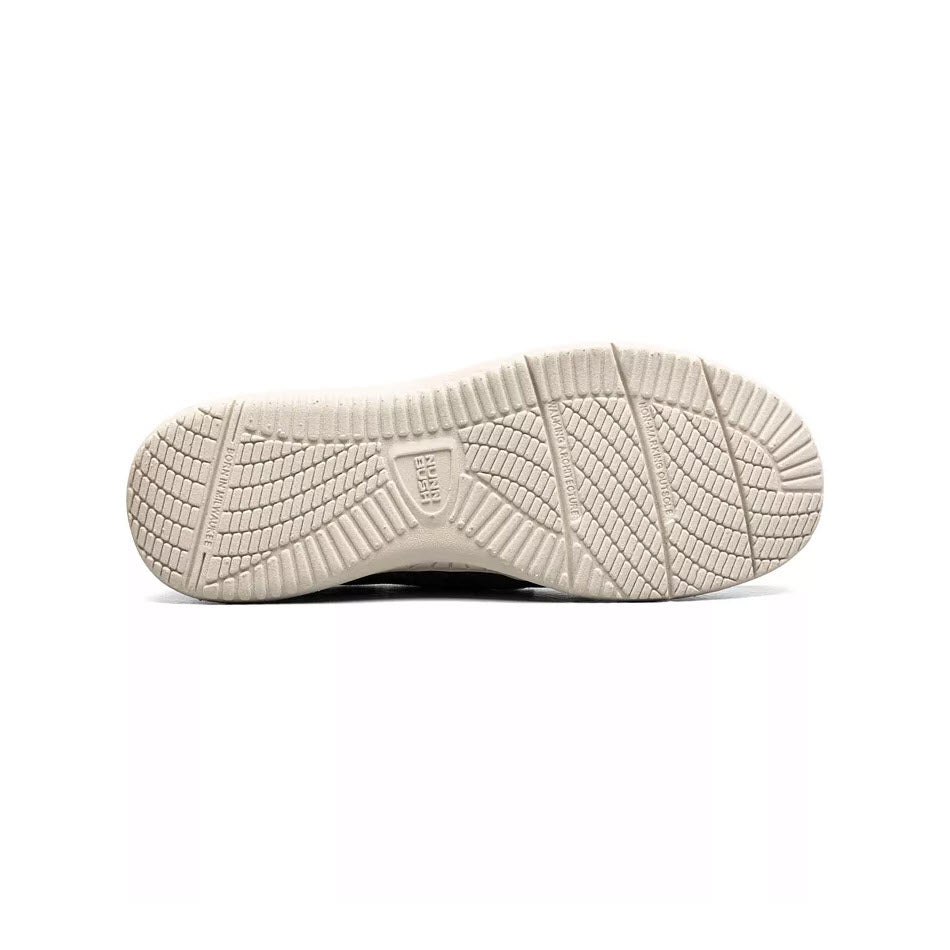 A close-up of the textured sole of a Nunn Bush Conway EZ Canvas Moc Toe Slip On Stone sneaker, showing patterns and brand logo, isolated on a white background.