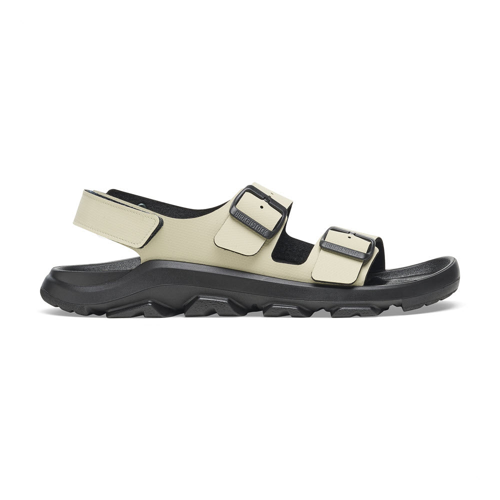 Side view of a beige and black Birkenstock BIRKENSTOCK MOGAMI TERRA OASIS EUCALYPTUS - WOMENS with two adjustable buckle straps and a velcro strap at the back. The sole has a rugged design, offering both flexibility and durability.