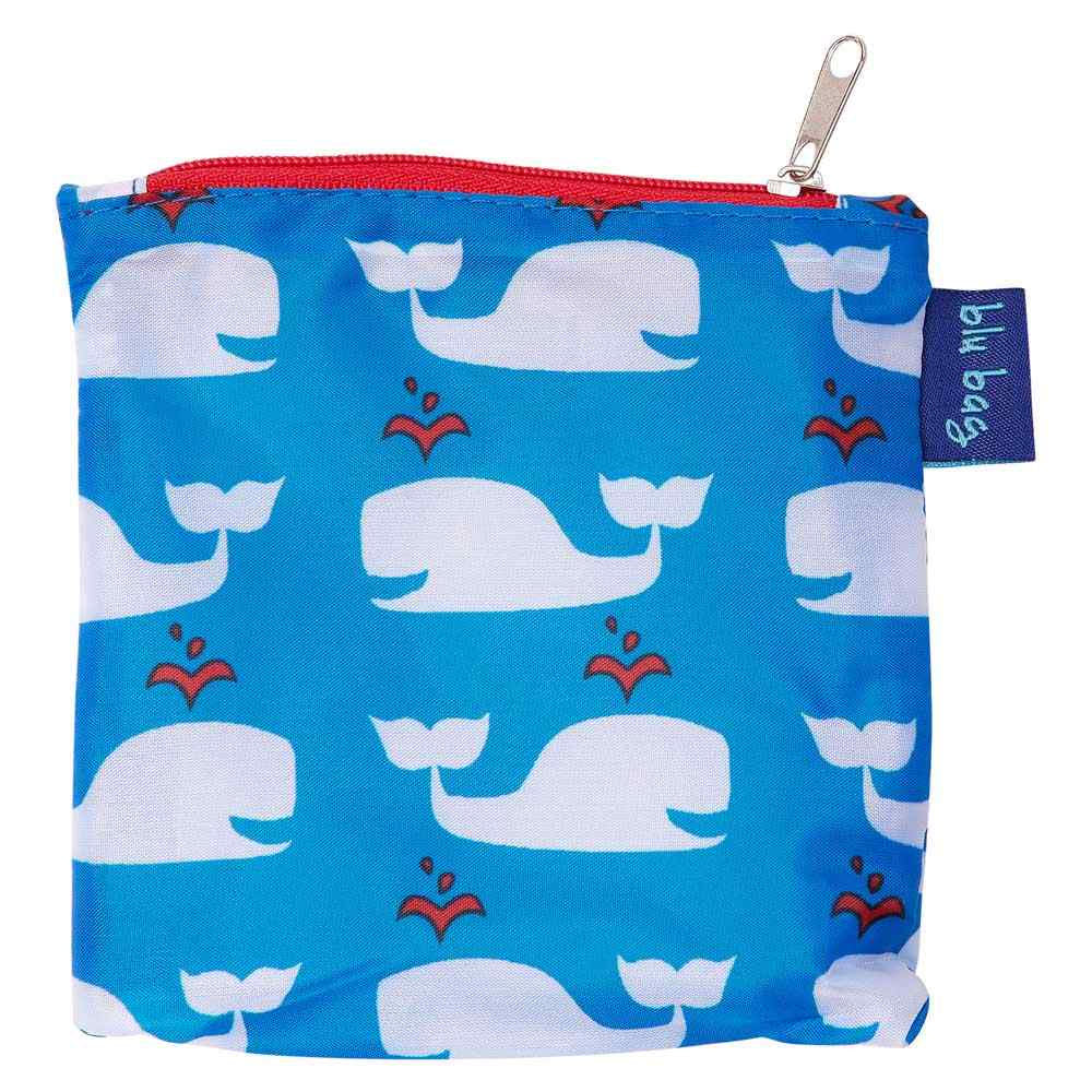 A Rockflowerpaper BLU BAG WHALES BLUE reusable shopping bag with a repeating pattern of white whales, featuring a red zipper and a brand tag on the side.