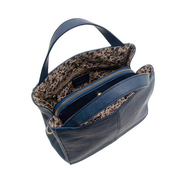A stylish blue JOY SUSAN BRANDI crossbody bag with a floral patterned interior, shown open to display internal compartments and a zippered section.
