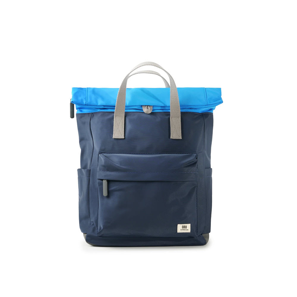 A Ori London ORI CANFIELD B MEDIUM NYLON MIDNIGHT BLUE commuter bag with a bright blue roll-top, short gray handles, and front pockets, set against a white background.