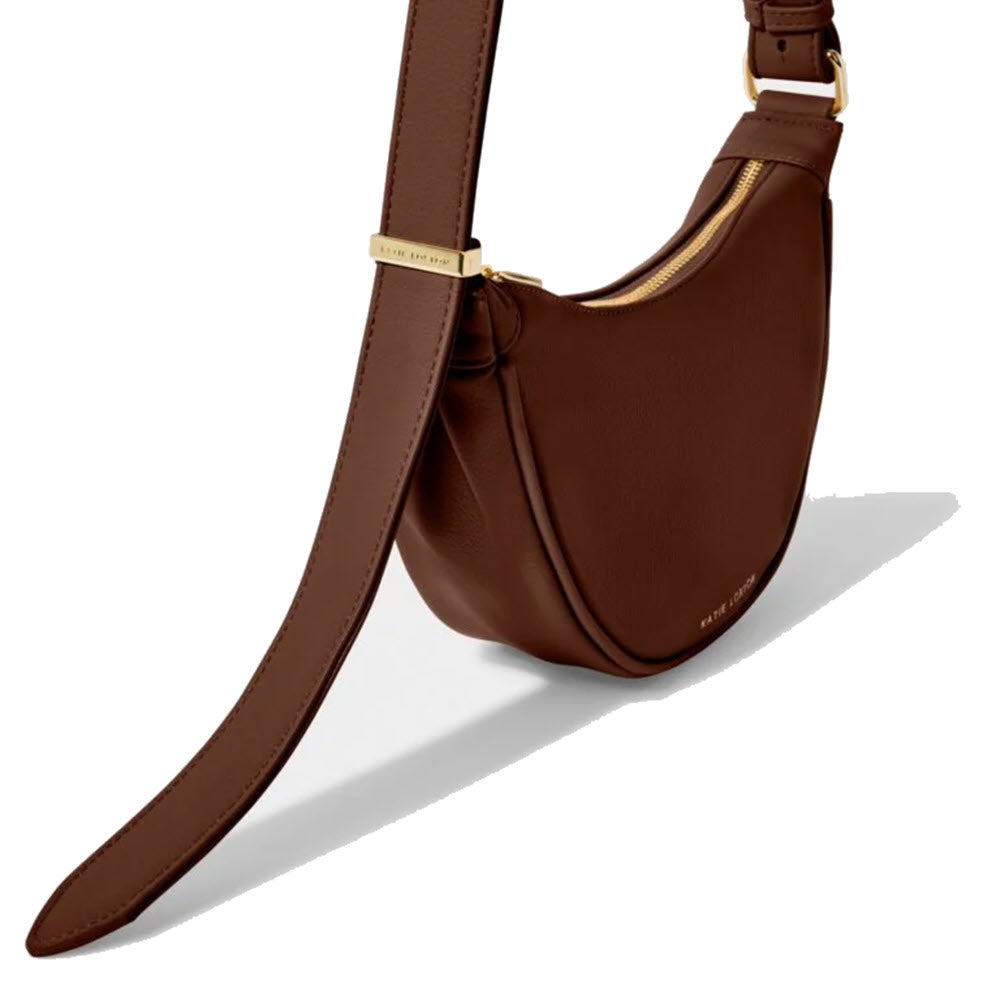 Brown vegan leather crescent-shaped Katie Loxton Harley Sling Chocolate with gold-tone hardware and crossbody strap.