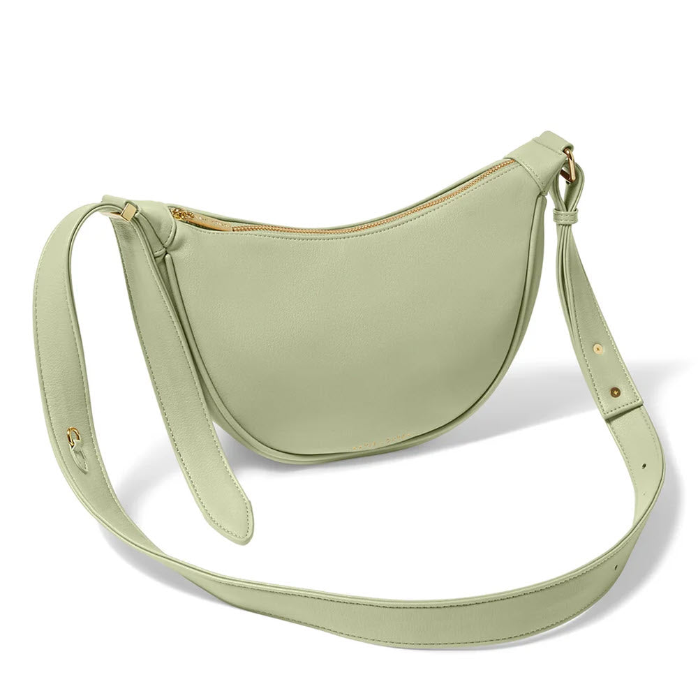 A soft sage vegan leather crescent-shaped Katie Loxton Harley Sling Bag with an adjustable strap and gold-tone hardware.