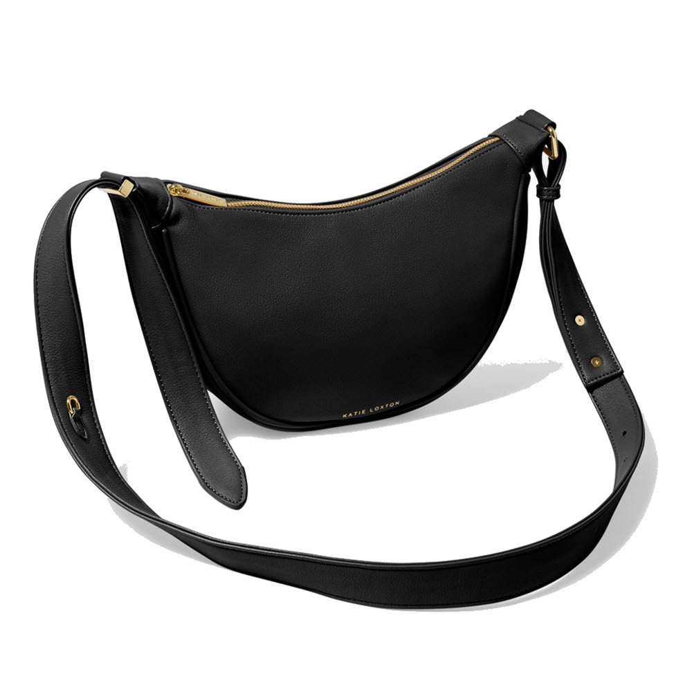 Black vegan leather crescent-shaped Katie Loxton Harley Sling Saddle Bag with an adjustable crossbody strap on a white background.