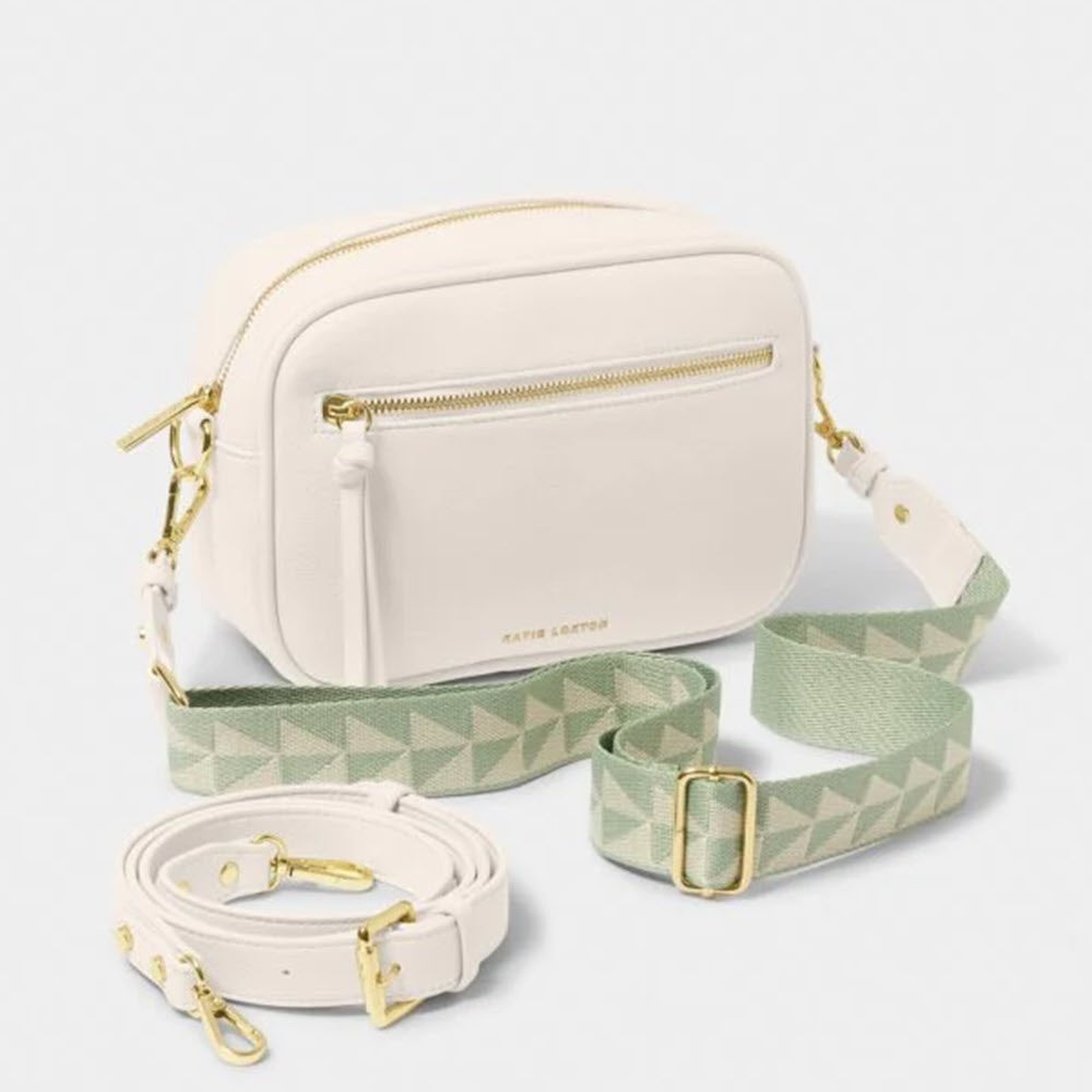 A small, white Katie Loxton Hallie crossbody bag made of vegan leather with a detachable geometric-patterned green strap and an additional plain white strap, positioned on a light background.