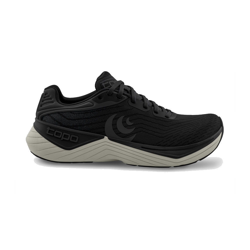 The TOPO ULTRAFLY 5 BLACK/CHARCOAL by Topo is a mens running shoe featuring a textured upper, gray sole, and brand logos, shown in side profile on a white background. Designed for enhanced cushioning and pronation support.