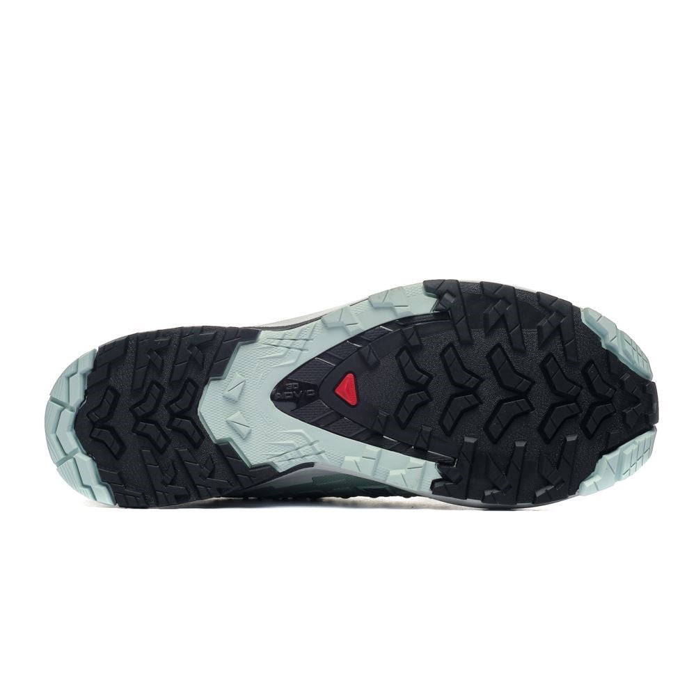 The sole of a hiking shoe featuring a black and gray tread pattern with a red triangular logo on a white background, designed for rugged grip - Salomon XA PRO 3D V9 Quiet Shade/Lily Pad/Blue Haze - Womens.
