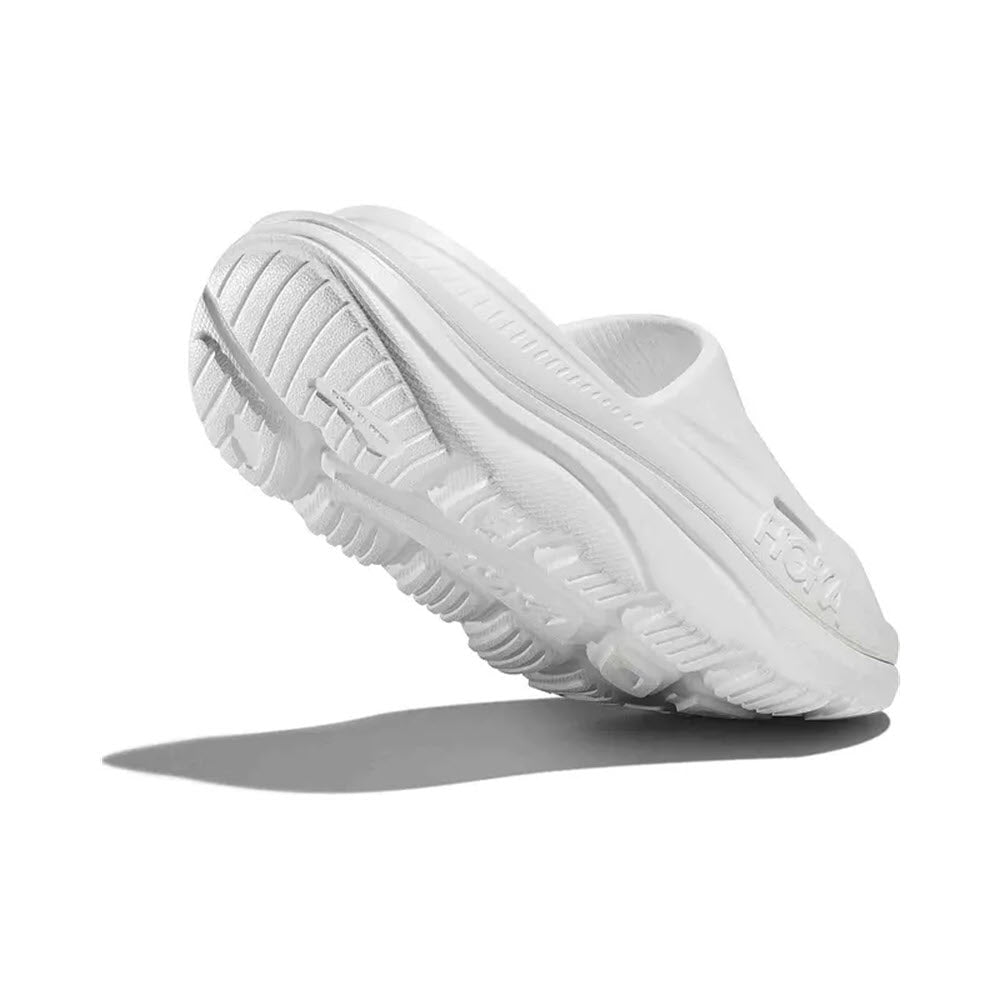 A white Hoka Ora Recovery Slide 3 sneaker with textured sole and sugarcane footbed, displayed with a raised heel on a plain background, casting a shadow.