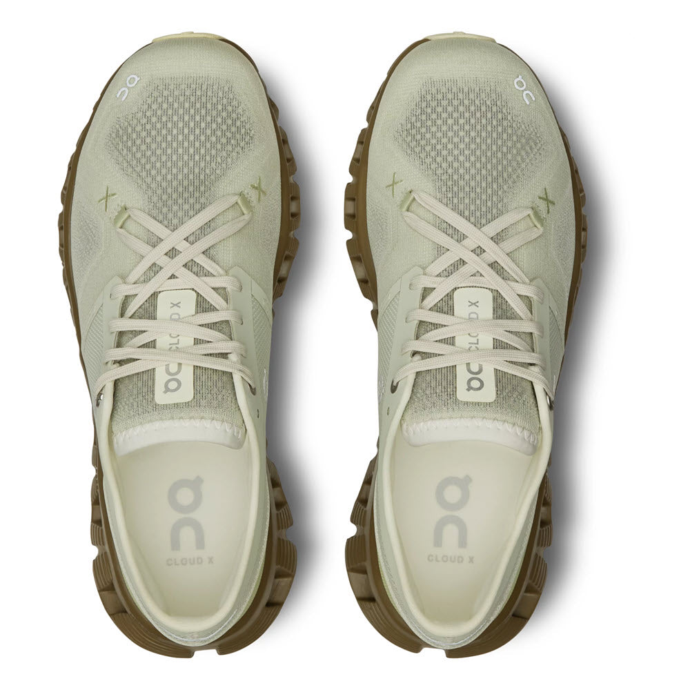 Top view of a pair of light beige running shoes with green accents, featuring prominent &quot;ON CLOUD X ALOE/HUNTER&quot; branding on the sole.