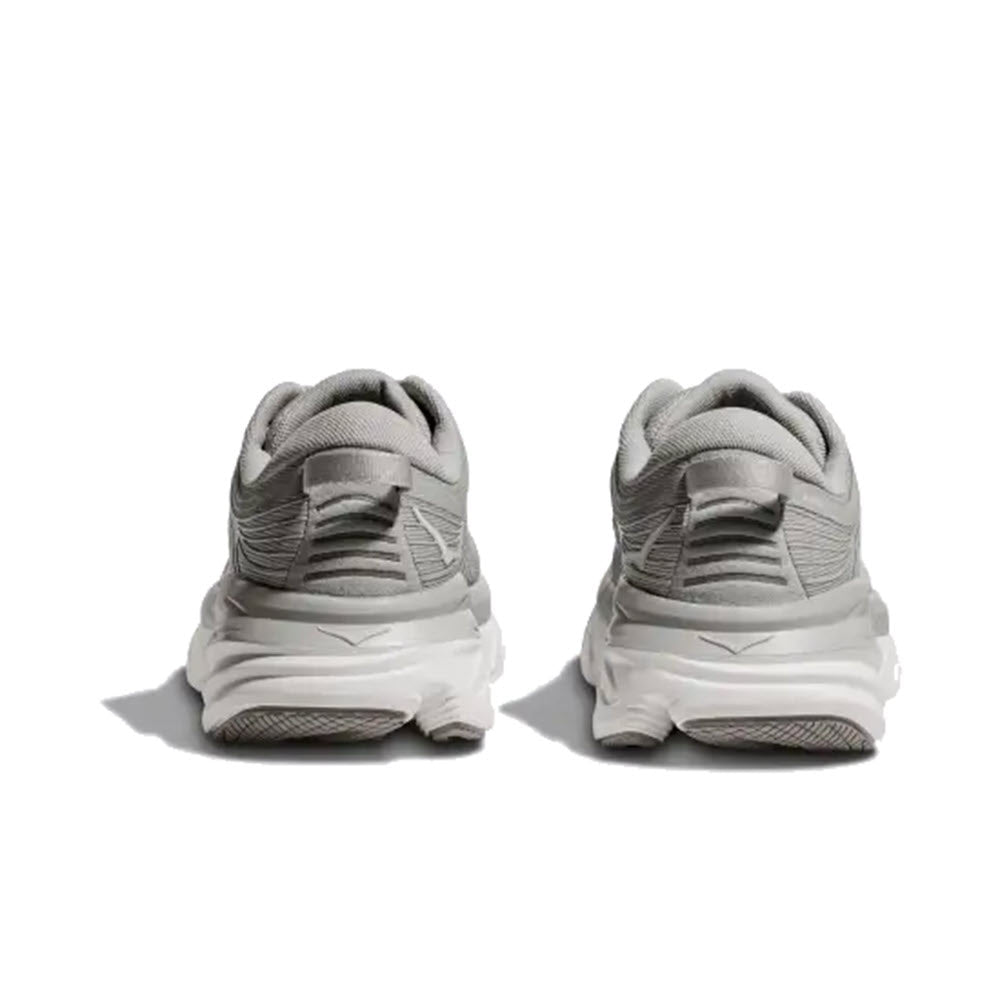 Rear view of a pair of gray Hoka HOKA BONDI 7 HARBOR MIST - WOMENS athletic shoes with white soles, placed side by side, showcasing the Meta-Rocker technology designed for enhanced comfort and performance.