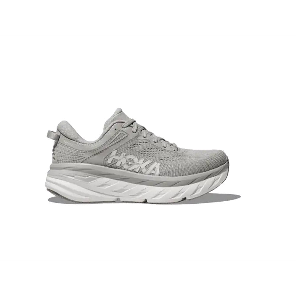 A single grey Hoka road shoe with a white, thick, cushioned sole featuring Meta-Rocker technology is displayed. The brand logo is visible on the side of the HOKA BONDI 7 HARBOR MIST - WOMENS. The shoe is photographed against a white background.