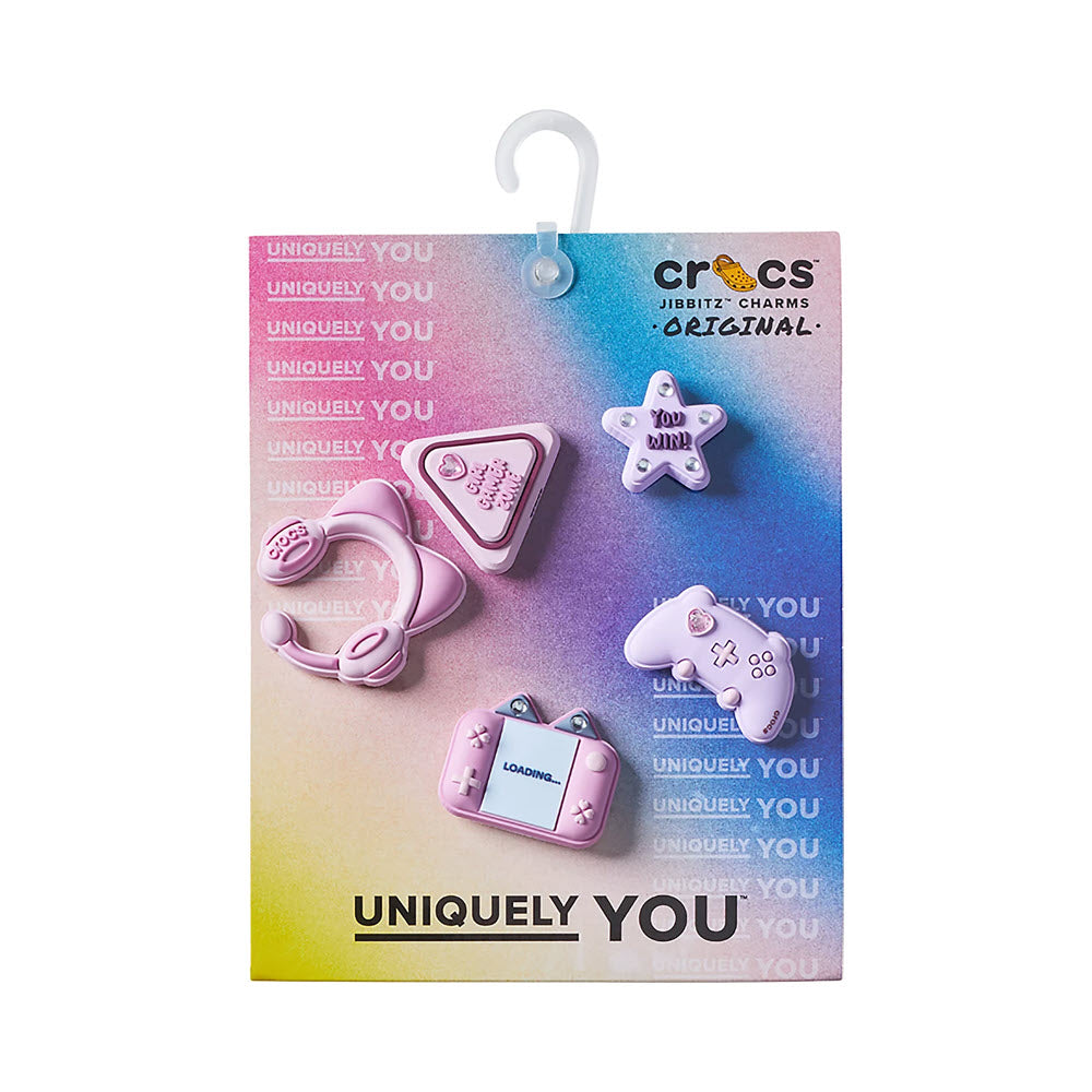 The JIBBITZ GIRL GAMER 5PACK by Jibbitz features five pastel purple charms—a headset, game controller, star, handheld console, and Gamer sign—for Crocs on gradient packaging with UNIQUELY YOU and CROCS Jibbitz Charms Original text.