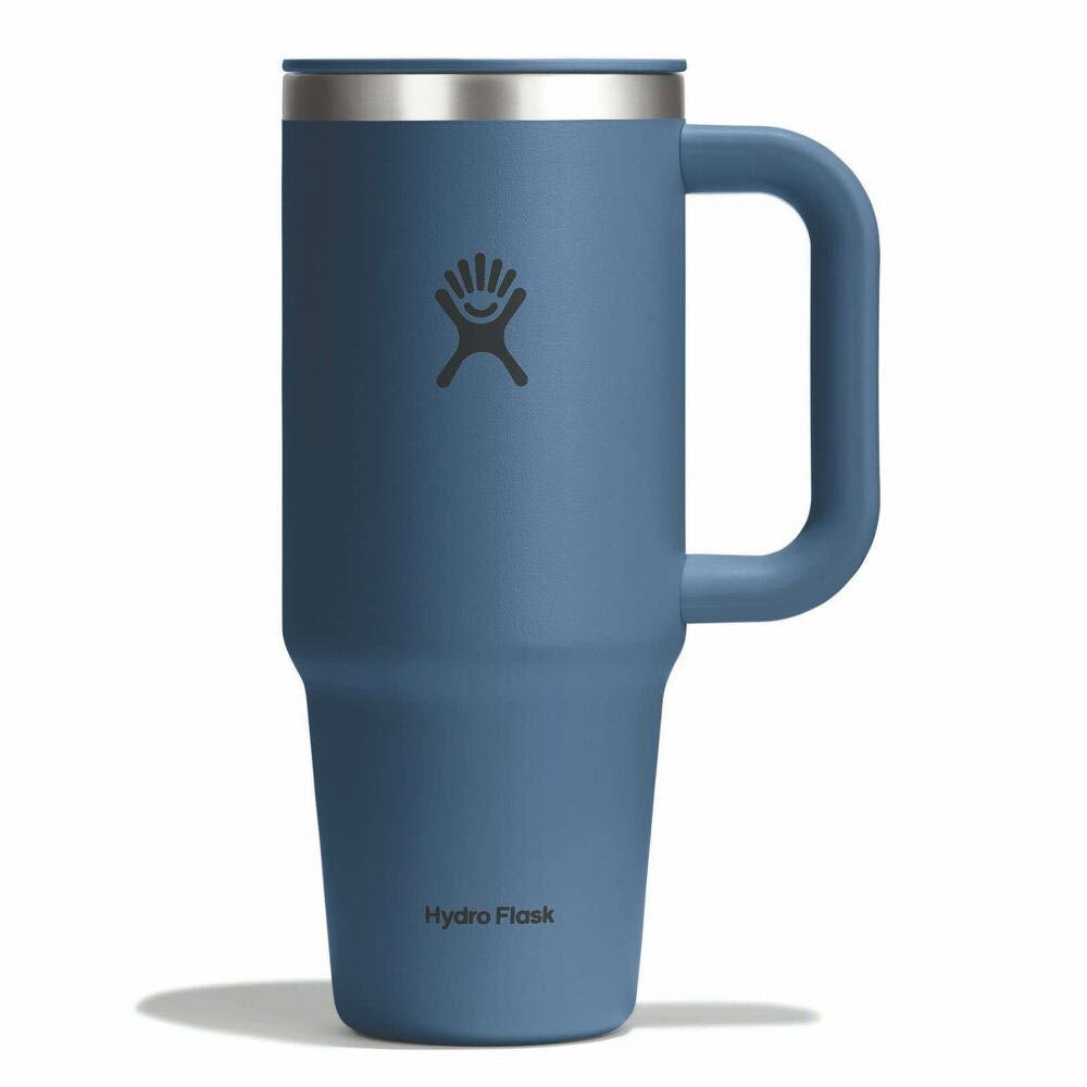 A blue Hydro Flask travel mug with a handle, a matte finish, and a black logo on the front. The mug has a silver rim at the top and casts a faint shadow on a white background.