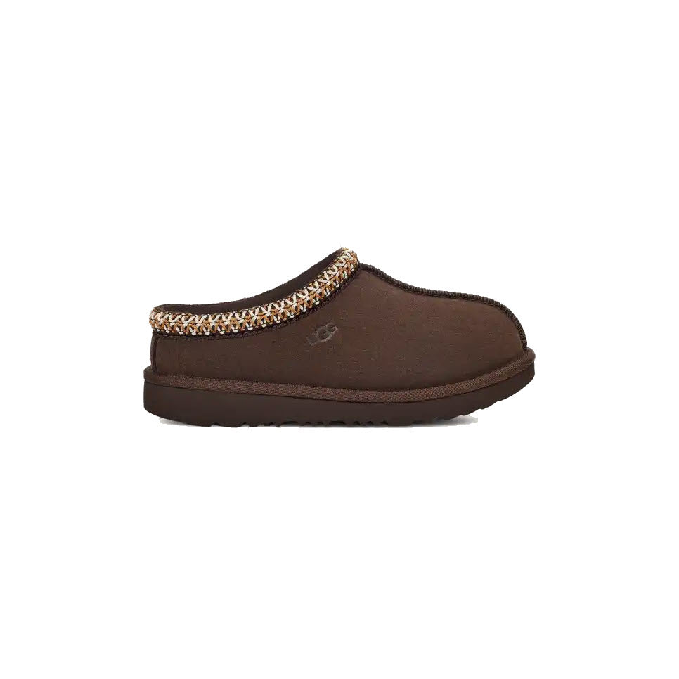 Brown suede slip-on slipper with a patterned trim around the opening, thick sole, and the UGG logo embroidered on the side, shown in a side profile view on a white background.