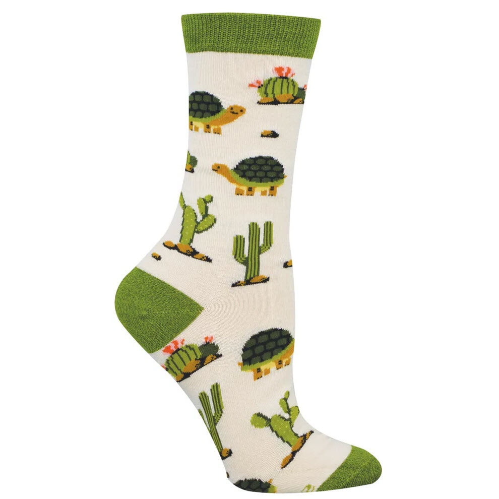 Cream-colored sock with green heel, toe, and cuff, featuring a playful pattern of turtles and cacti with small pink flowers.