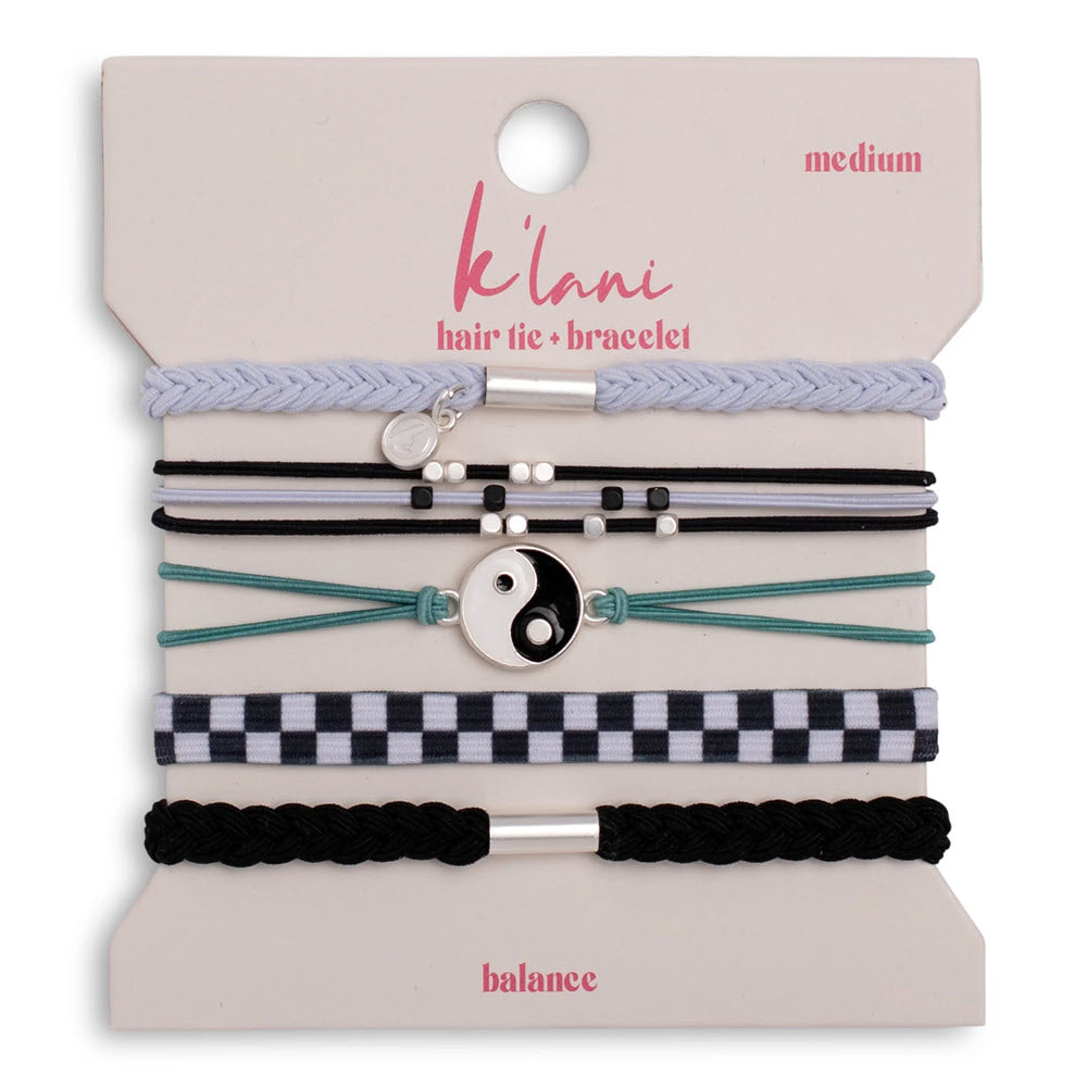 Five assorted hair ties and bracelets on a card labeled klani. Designs include a braided lavender tie, black and white bands with beads, a yin-yang charm, a checkered band, and a black braided tie with a silver bar.