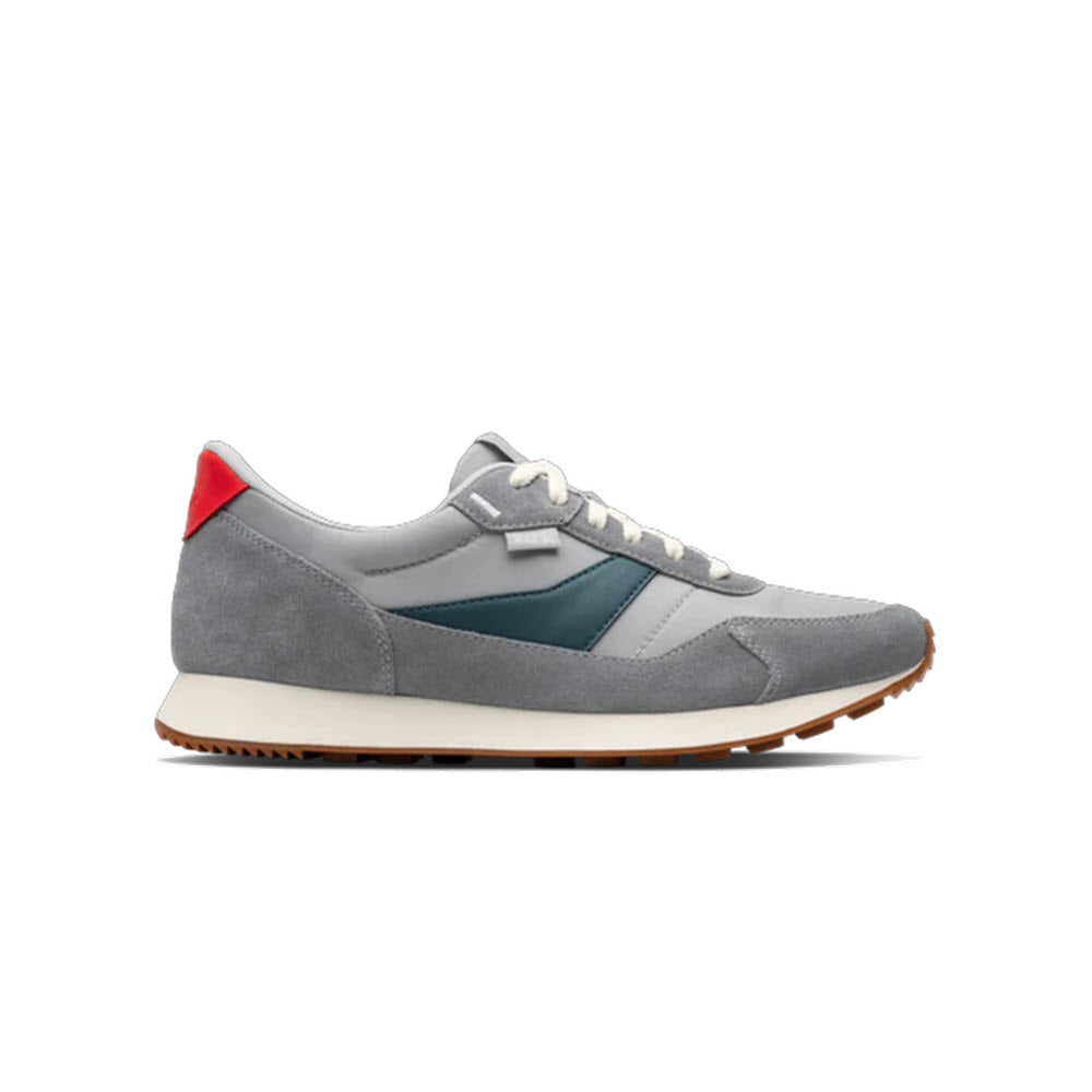 A grey sneaker with white laces, a dark green accent on the side, a white midsole, a brown outsole, and a small red detail on the heel.