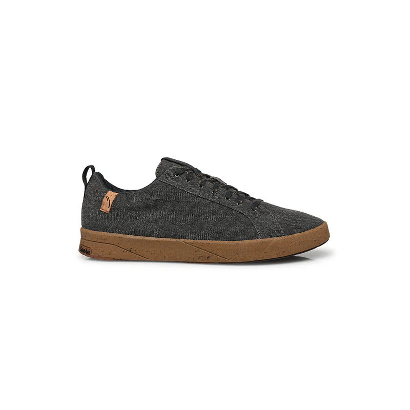 A charcoal grey low-top sneaker with a brown rubber sole, black laces, and a small tan logo tag on the collar near the heel. The design is minimal and casual.