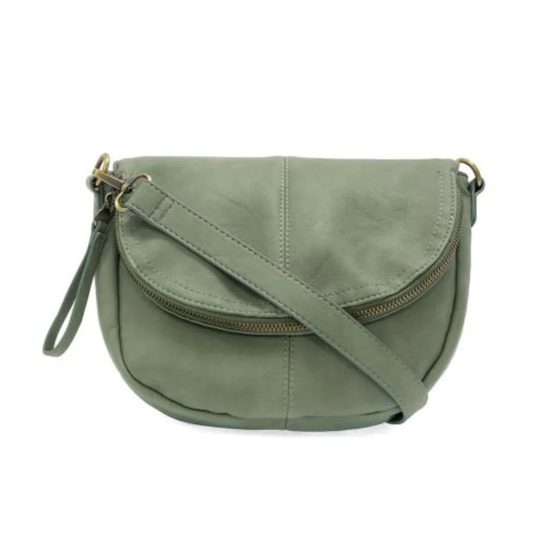 A small, sage green crossbody bag with a curved shape, front zipper pocket, and an adjustable strap. The bag has a smooth texture and a wristlet strap attached to one side.