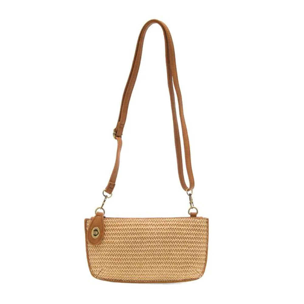 A small rectangular woven straw crossbody bag with a tan adjustable leather strap and gold hardware, featuring a leather tag detail on one side.
